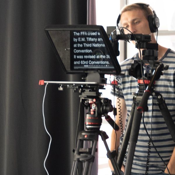 Chad standing behind a teleprompter and camera shooting a video. 
